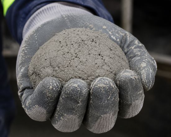 A gloved hand holds a mound of wet concrete or cement mixture, demonstrating its texture and mortar consistency up close—an observation often performed during the Ball-in-Hand Test following ASTM C860 standards.